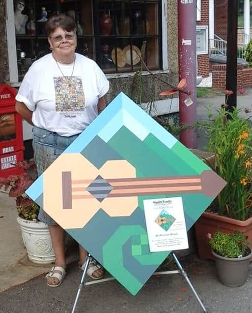 Carole Pearson with a guitar barn quilt in front of One of a Kind Art Gallery. Photo by Carole Pearson.