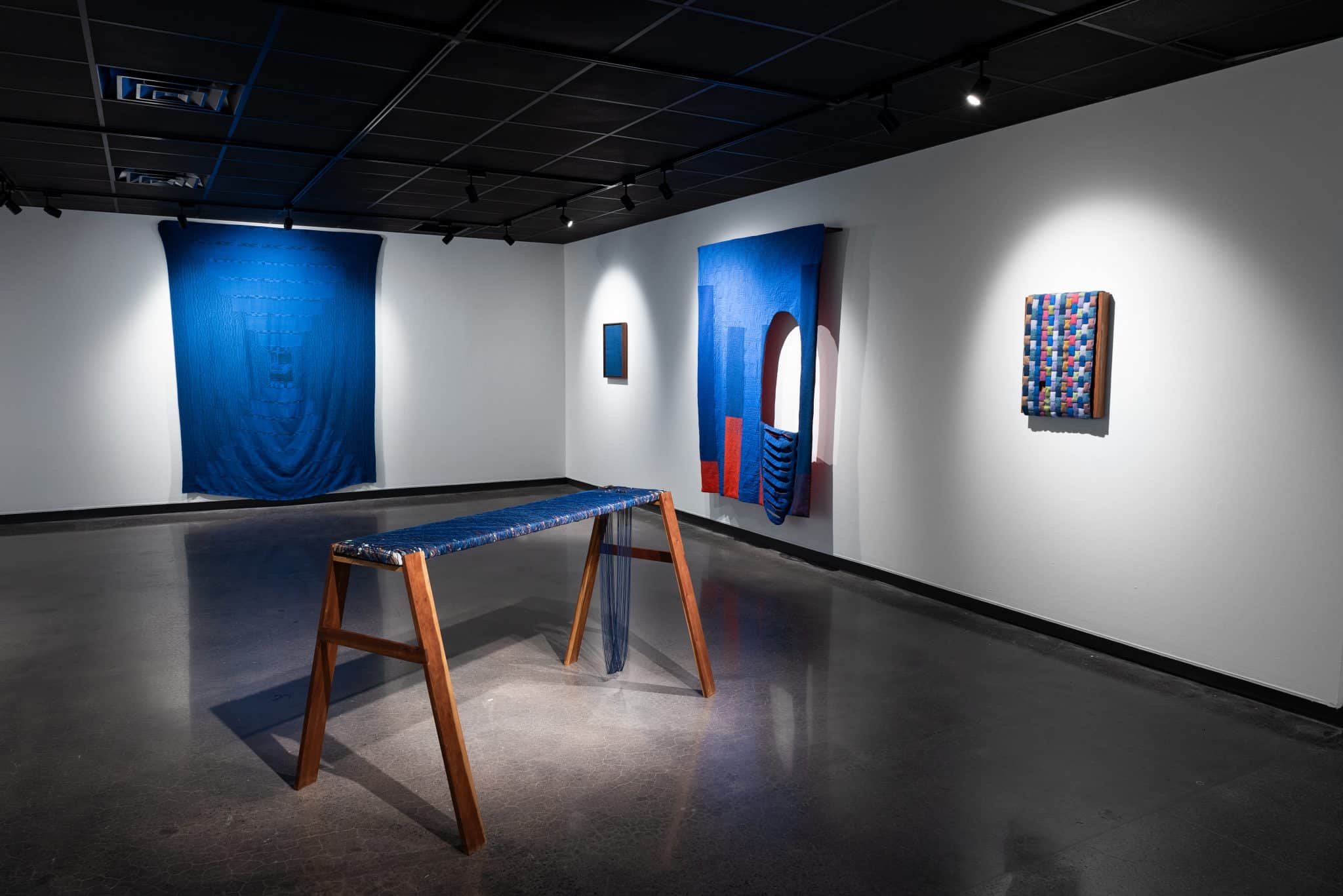 Photo of art studio with several weavings on the wall and a bench 