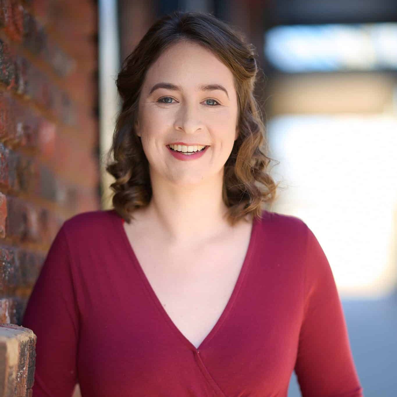 Woman smiling, wearing a rust colored v-neck sweater