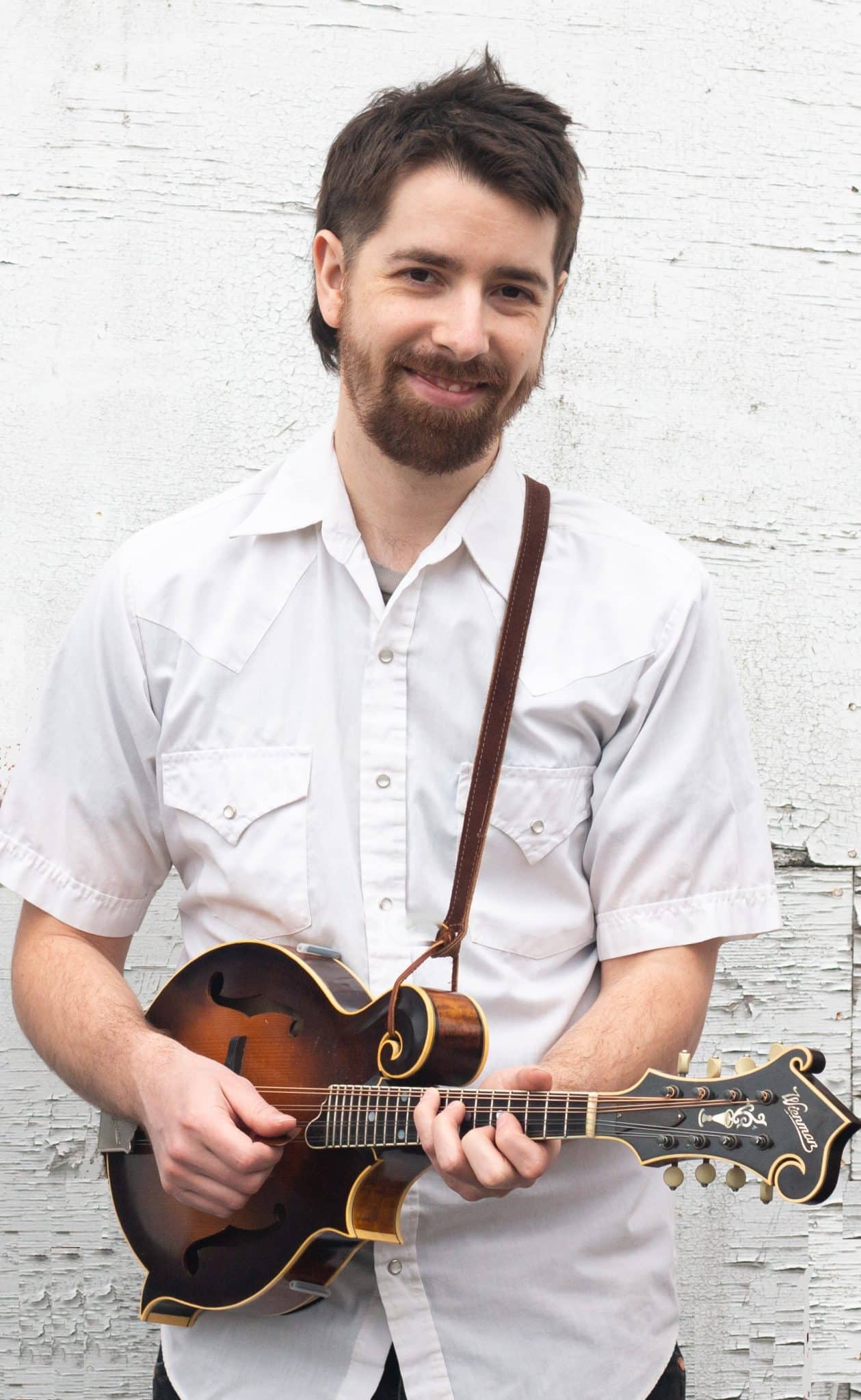 Image of a man playing a stringed instrument, wearing a white button up shirt